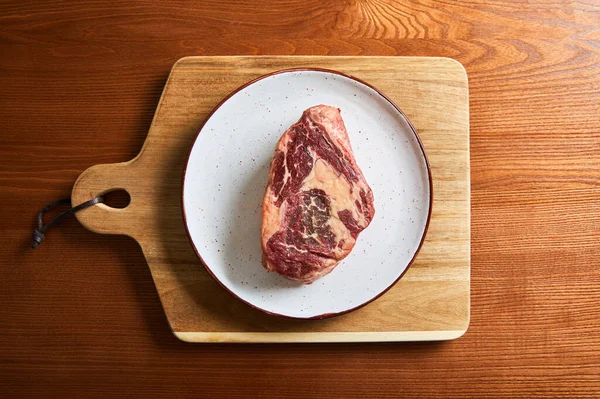 Top view of fresh raw steak on plate on cutting board on wooden table — Stock Photo