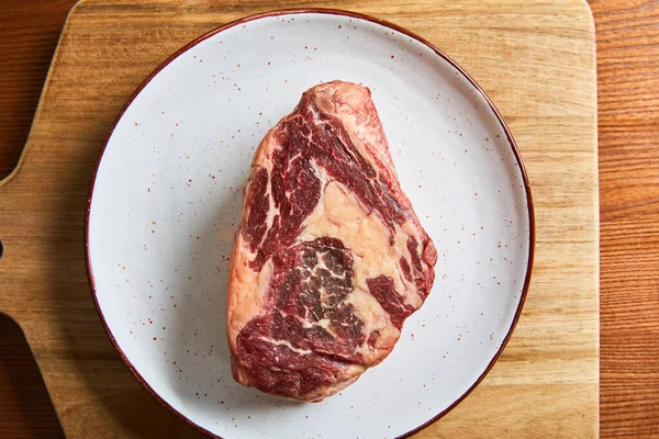 Top view of fresh raw steak on plate on cutting board on wooden table — Stock Photo