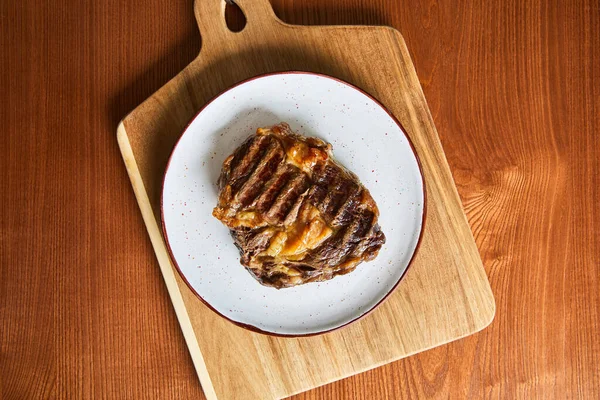 Vue du dessus du steak frais grillé sur plaque sur planche à découper sur table en bois — Photo de stock