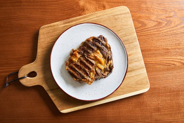 Vue du dessus du steak frais grillé sur plaque sur planche à découper sur table en bois — Photo de stock