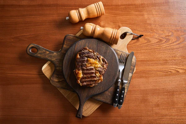 Top view of tasty grilled steak served on wooden boards with cutlery, salt and pepper mills — Stock Photo