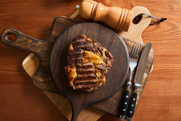 Blick von oben auf leckeres Steak vom Grill, serviert auf Holzbrettern mit Besteck, Salz- und Pfeffermühlen — Stockfoto