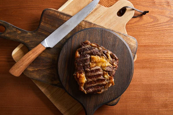 Вид сверху на вкусный жареный стейк, подаваемый на деревянных досках с ножом — стоковое фото