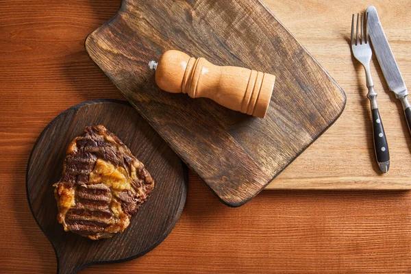 Top view of tasty grilled steak served on wooden boards with cutlery and salt mil — Stock Photo