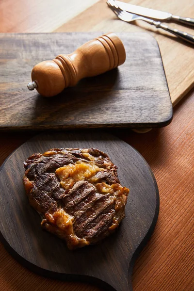 Selective focus of tasty grilled steak served on wooden boards with cutlery and salt mil — Stock Photo