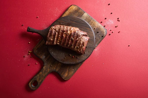 Top view of tasty grilled steak served on wooden boards on red background with pepper and salt — Stock Photo