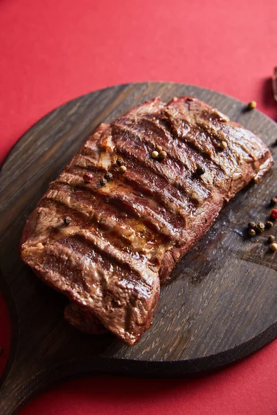 Tasty grilled steak served on wooden boards on red background with pepper — Stock Photo