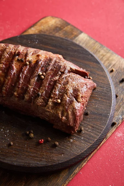 Tasty grilled steak served on wooden boards on red background with pepper and salt — Stock Photo