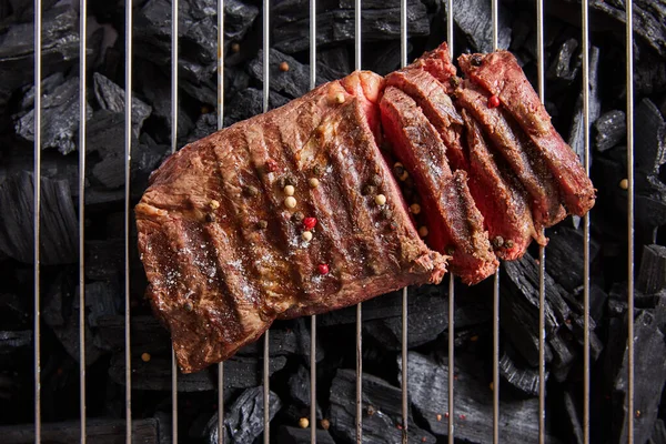 Vista superior de corte fresco grelhado saboroso bife com assadura rara e condimentos na grelha acima de carvão preto — Fotografia de Stock