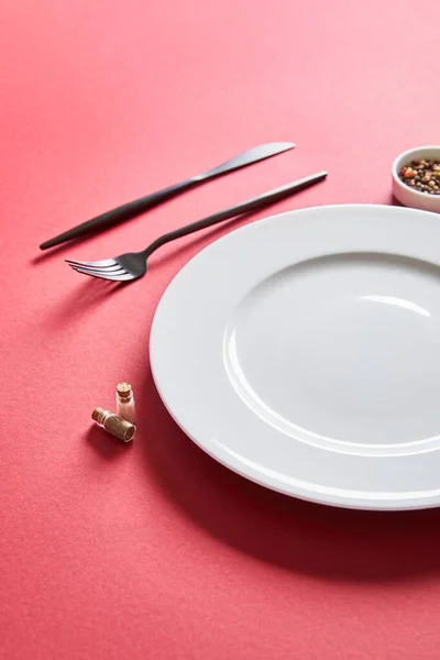 Empty round plate with cutlery and pepper in bowl on red background — Stock Photo