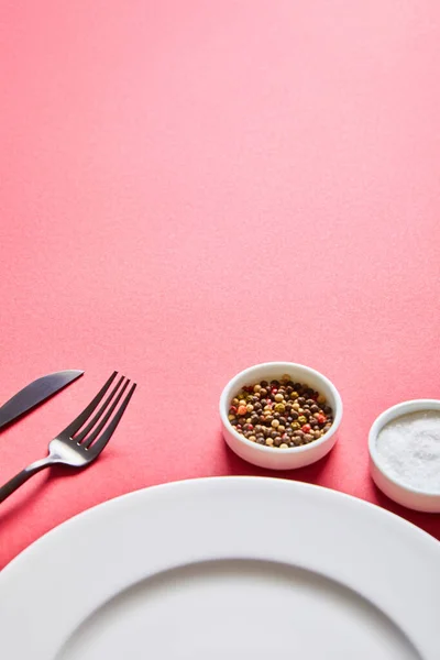 Leere runde Platte mit Besteck und Salz und Pfeffer in Schüsseln auf rotem Hintergrund — Stockfoto