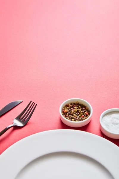 Assiette ronde vide avec couverts et sel et poivre dans des bols sur fond rouge — Photo de stock