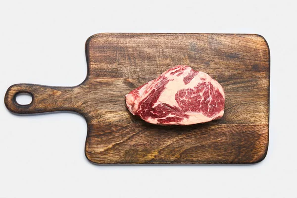 Draufsicht auf frisches rohes Steak auf hölzernem Schneidebrett auf weißem Hintergrund — Stockfoto