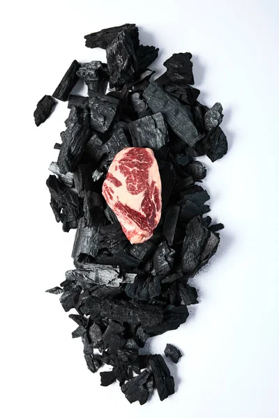 Vue de dessus du steak cru frais sur les charbons noirs sur fond blanc — Photo de stock