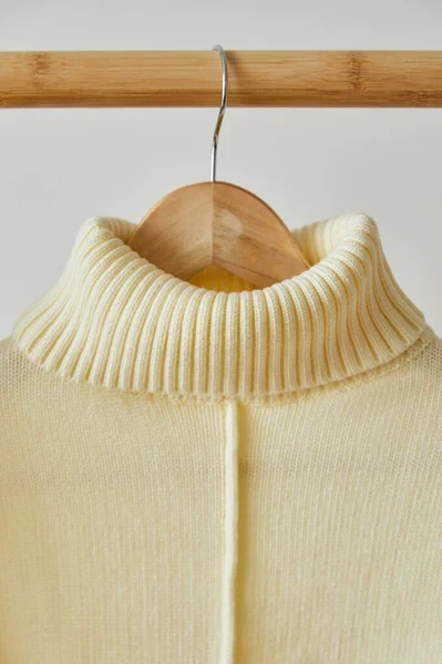 Close up view of beige knitted soft sweater hanging on wooden hanger isolated on white — Stock Photo