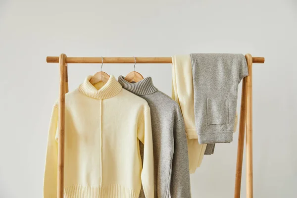 Beige and grey knitted soft sweaters and pants hanging on wooden hangers isolated on white — Stock Photo