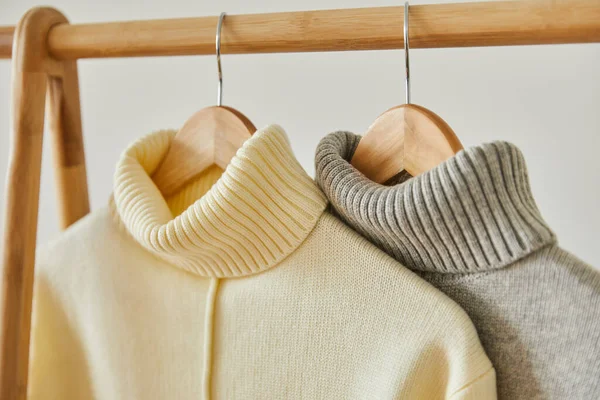 Close up view of beige and grey knitted soft sweaters hanging on wooden hangers isolated on white — Stock Photo