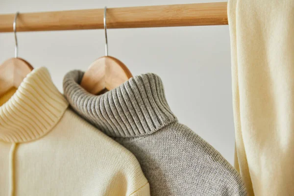 Close up view of beige and grey knitted soft sweaters hanging on wooden hangers isolated on white — Stock Photo