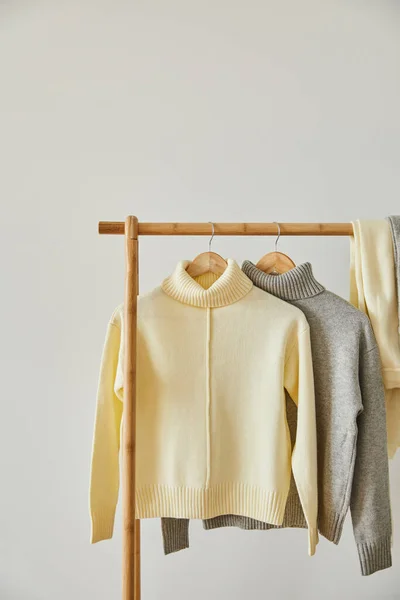 Beige und grau gestrickte weiche Pullover hängen an hölzernen Kleiderbügeln isoliert auf weiß — Stockfoto