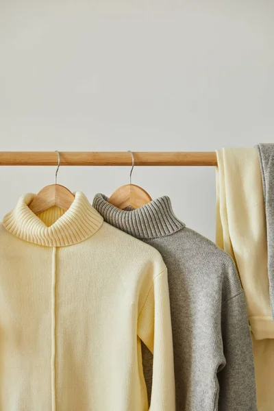 Chandails doux tricotés beige et gris suspendus à des cintres en bois isolés sur blanc — Photo de stock