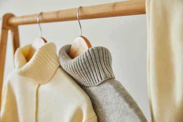Enfoque selectivo de suéteres suaves de punto beige y gris que cuelgan de perchas de madera aisladas en blanco - foto de stock