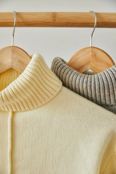 Close up view of beige and grey knitted soft sweaters hanging on wooden hangers isolated on white — Stock Photo