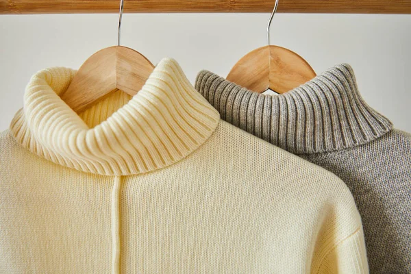 Close up view of beige and grey knitted soft sweaters hanging on wooden hangers isolated on white — Stock Photo