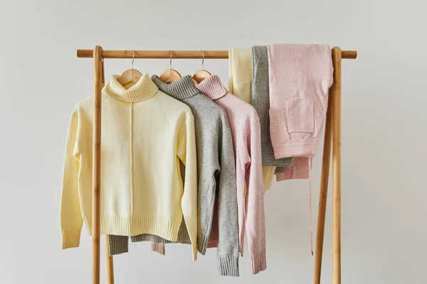 Pulls doux tricotés rose, beige et gris et pantalons suspendus sur un support en bois isolé sur du blanc — Photo de stock