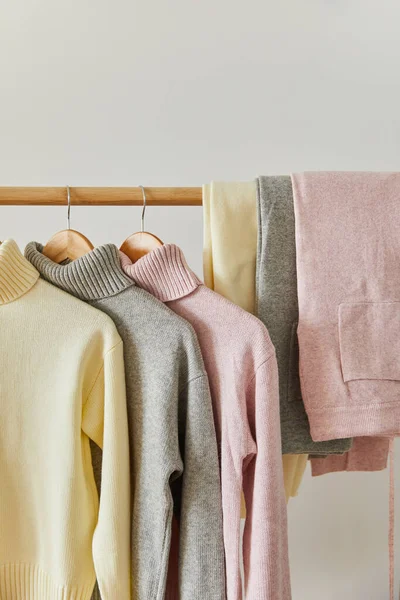 Close up view of pink, beige and grey knitted soft sweaters and pants hanging on wooden rack isolated on white — Stock Photo