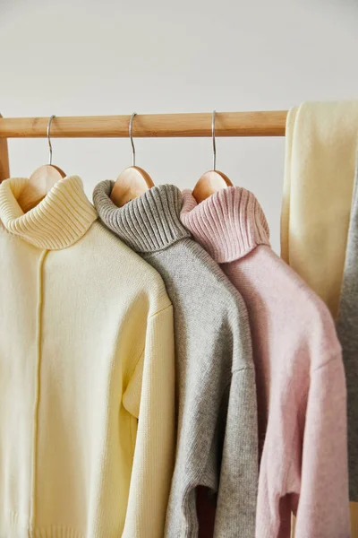 Close up view of pink, beige and grey knitted soft sweaters and pants hanging on wooden rack isolated on white — Stock Photo