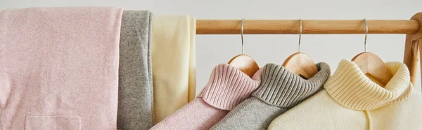 Close up view of pink, beige and grey knitted soft sweaters and pants hanging on wooden rack isolated on white, panoramic shot — Stock Photo