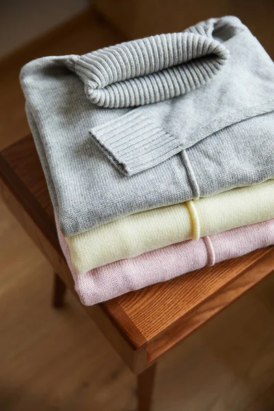 Vue rapprochée des pulls doux en maille rose, beige et gris sur une table en bois dans la chambre — Photo de stock