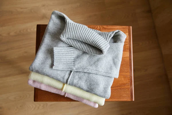 Vue de dessus des pulls doux en maille rose, beige et gris sur la table en bois dans la chambre — Photo de stock