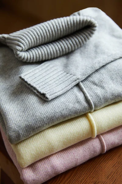 Close up view of pink, beige and grey knitted soft sweaters on wooden table in room — Stock Photo