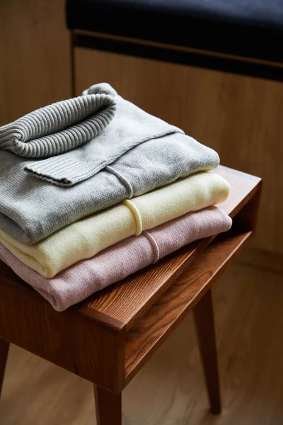 Suéteres suaves de punto rosa, beige y gris sobre mesa de madera en la habitación - foto de stock