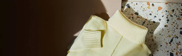 Top view of yellow knitted soft sweater on stone and paper surface in sunlight, panoramic shot — Stock Photo