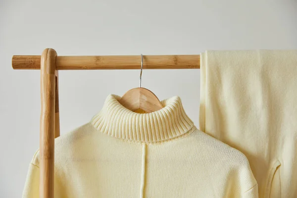 Close up view of beige knitted soft sweater and pants hanging on wooden hanger isolated on white — Stock Photo