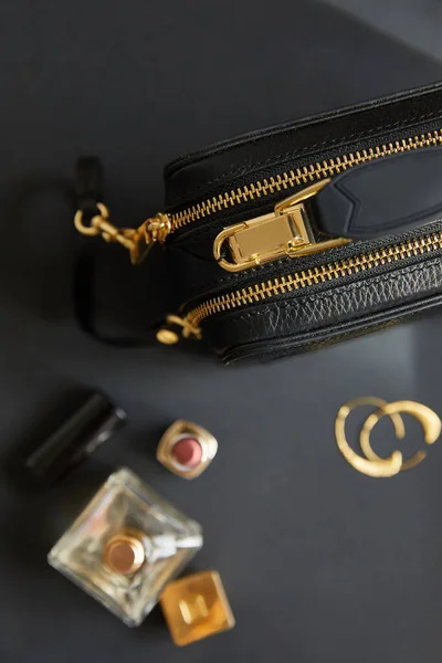 Top view of leather handbag near golden earrings, perfume and lipstick on black table — Stock Photo