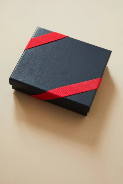 Black gift box with red ribbon on beige background — Stock Photo