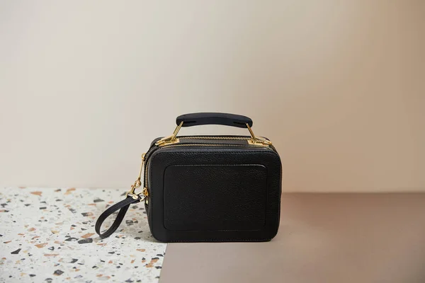 Шкіряна чорна сумка з золотими блискавками на мармуровій поверхні на бежевому фоні — стокове фото