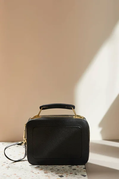 Bolso de mano de cuero negro con cremalleras doradas en superficie de mármol sobre fondo beige — Stock Photo