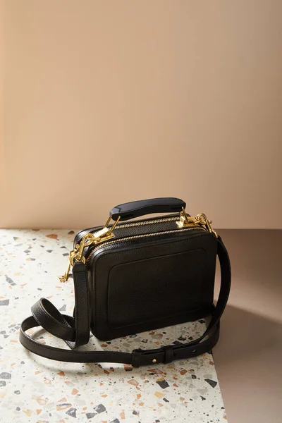 Leather black handbag with golden zippers on marble surface on beige background — Stock Photo