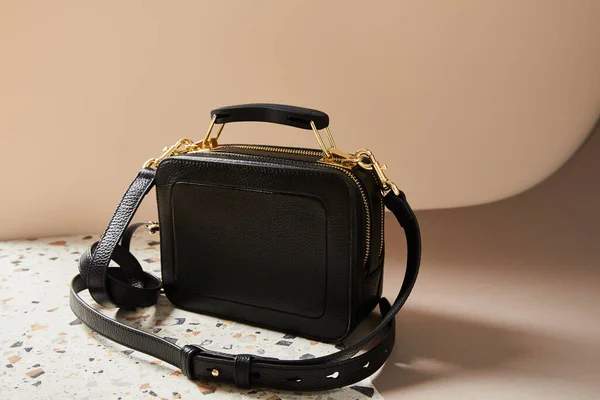 Schwarze Lederhandtasche mit goldenen Reißverschlüssen auf Marmoroberfläche auf beigem Hintergrund — Stockfoto