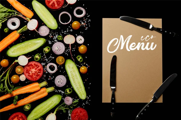 Vue du dessus des tranches de légumes frais avec sel près de la carte de papier avec illustration de menu et couteaux isolés sur noir — Photo de stock