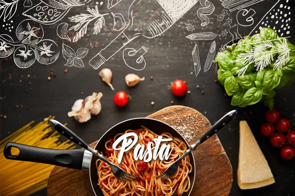 Top view of tasty bolognese pasta in frying pan near ingredients and cutlery on black wooden background, food illustration — Stock Photo