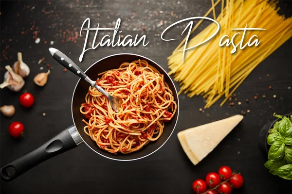 Selective focus of tasty bolognese pasta in frying pan near ingredients on black wooden background, italian pasta illustration — Stock Photo