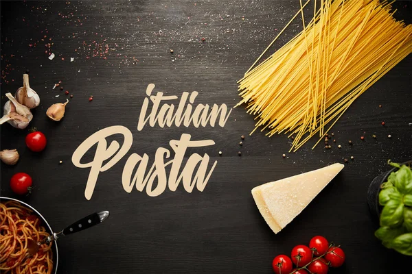 Vista superior de la deliciosa pasta boloñesa en sartén cerca de los ingredientes sobre fondo de madera negro, ilustración de pasta italiana - foto de stock