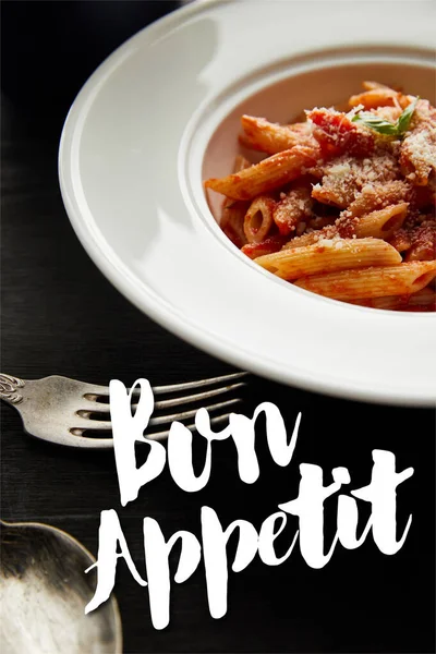 Tasty bolognese pasta with tomato sauce and Parmesan in white plate near cutlery on black wooden background, bon appetit illustration — Stock Photo