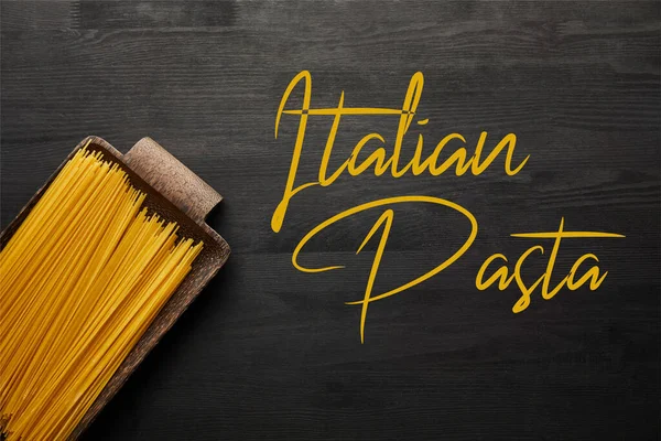 Top view of raw spaghetti on black wooden background, italian pasta illustration — Stock Photo