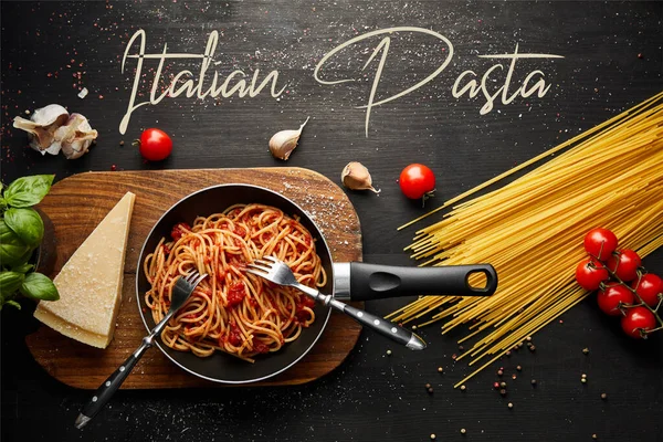 Vista dall'alto della gustosa pasta bolognese in padella vicino agli ingredienti e posate su fondo nero in legno, illustrazione pasta italiana — Foto stock